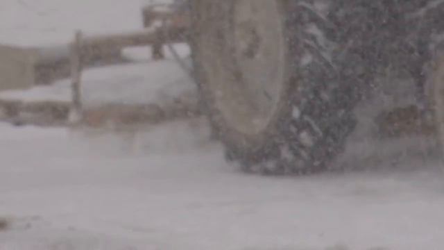 Зимний трактор чистит дорогу от снега в снег.