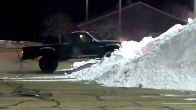 Lifted Jeep Comanche climbs snow pile in a parking lot