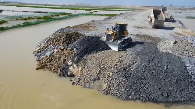 Строительство дороги в заболоченной местности. Бульдозеры отсыпают дорогу, самосвалы подвозят грунт