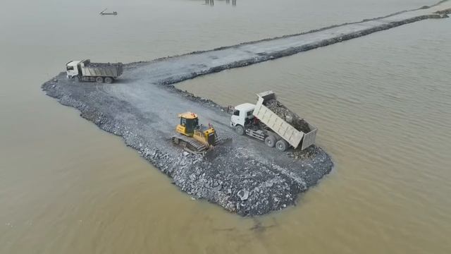 Строительство дороги на воде. Самосвалы подвозят грунт, бульдозер отсыпает дорогу