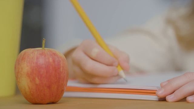 Close Up Of Child Writing In Book At Table With Apple In Foreground