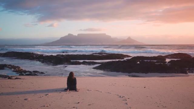 A Woman Seated On The Beach Sand Enjoying The Table Mountain View