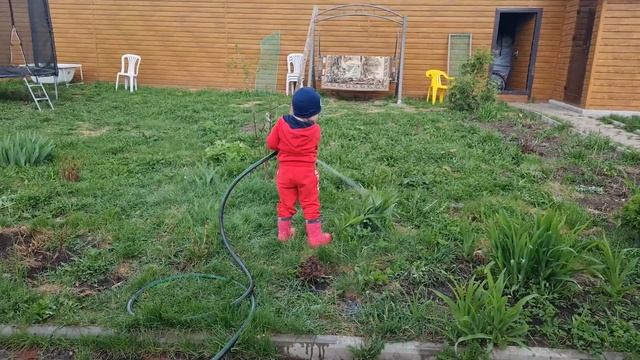 A child waters the grass in the garden with a hose