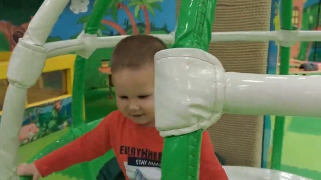 A child slides down a slide on a playground and plays catch in a pool with colored balls.