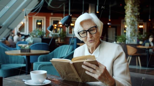 Smart senior business lady reading book at table in restaurant relaxing during coffee break