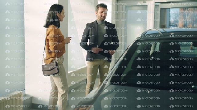 Attractive young woman talking to sales manager in car dealership choosing auto