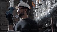 Engineer works in boiler room, dictates audio message on smartphone