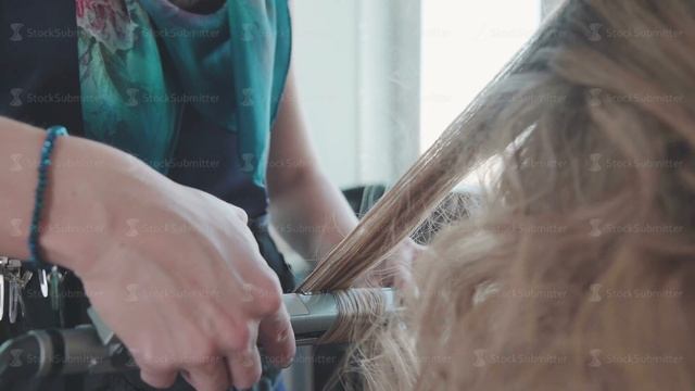 Hairdresser makes curls using a styler - a curling iron