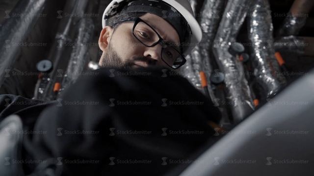Man with beard, wearing glasses, white helmet stands in a boiler room
