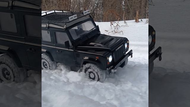 RC Land Rover Defender прорывается через снежные сугробы.