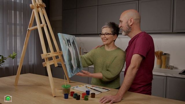 Talented mature female artist showing painting to loving man indoors
