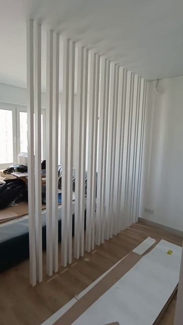 Белая реечная перегородка в спальне у кровати с разным расстоянием между брусьями