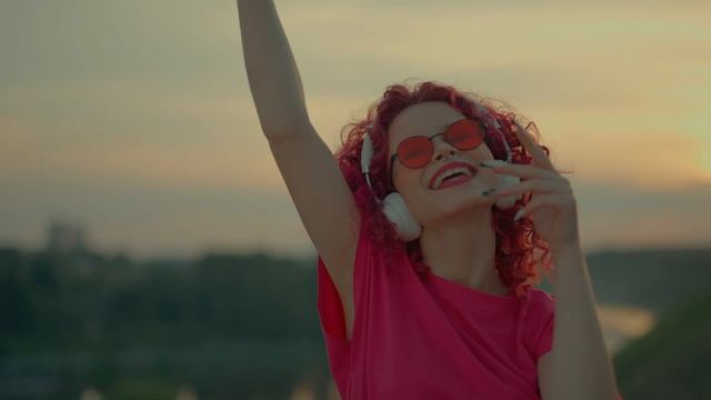 Кудрявая рыжеволосая девушка слушает музыку на улице