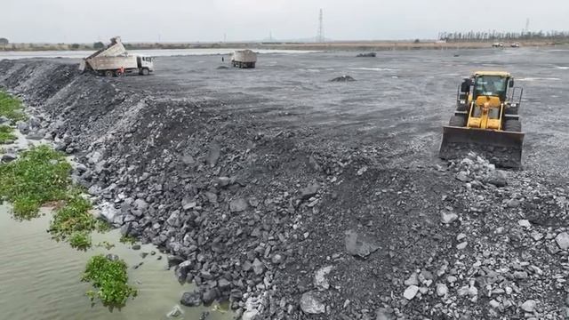 Грузовики, перевозящие большие камни в озеро, с колесным погрузчиком, толкающим камни