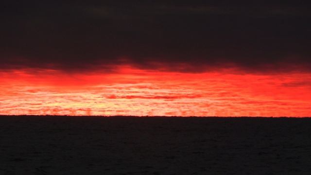 Огненное отражение заката в ледяных облаках на чернильно Чёрным морем.