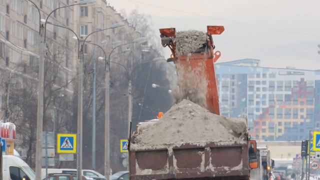 Снегоуборочный комбайн загружает снег в самосвал КамАЗ