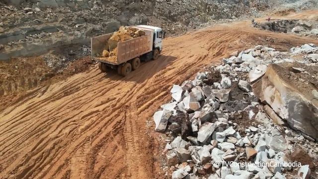 фундамент здания на горной дороге, оператор  бульдозера, самосвал разгружающий камни