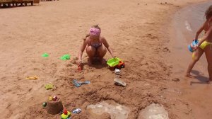 Девочки играют с машинками в песке на берегу моря