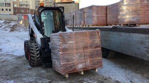 Разгрузка погрузчиком Bobcat кирпича на паллетах с прицепа