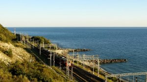 два пассажирских поезда едут навстречу  по железной дороге у склона горна берегу Черного моря в солн