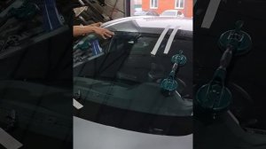 Мастер вклеивает лобовое стекло на автомобиль.