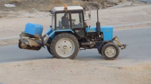 Трактор с Баком воды и Щёткой едет, чистит дорогу от грязи и пыли.