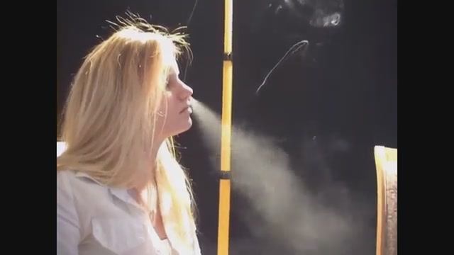 Blonde woman smokes, nose exhales.