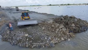 Строительство насыпной дороги на воде. Бульдозер разравнивает грунт, который привозят самосвалы