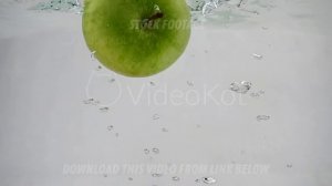 One green apple falls into the water with bubbles at a slow pace. Apple on isolated white backgroun