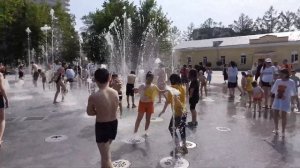 Funny children play with water in the fountain on a hot day