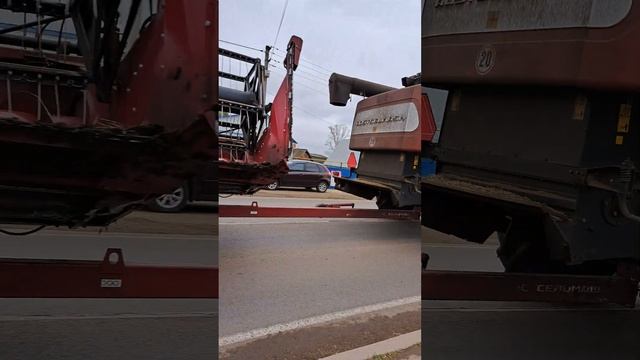 The combine is driving along the road, carrying the reaper behind it.
