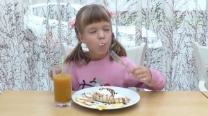 Девочка ест десерт из блинчика, мороженного и фруктов в кафе. Girl eating pancake ice-cream and fru