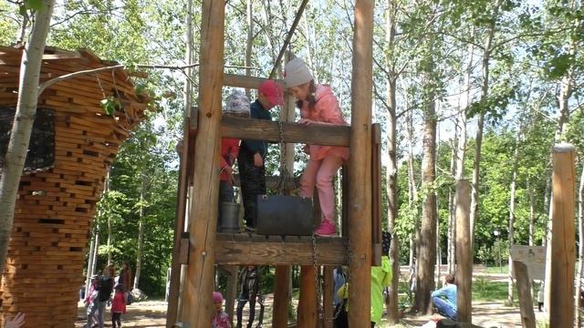 Дети играют на деревянной детской площадке, качаются на качелях. Веревочный парк.