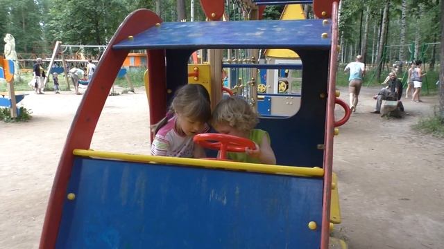 Дети катаются с горки, качаются на качелях на детской площадке в парке.