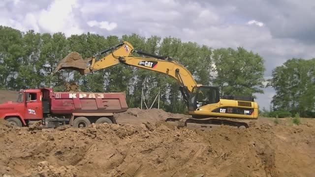 Экскаватор Cat 330D LME грузит самосвалы КрАЗ в глиняном карьере