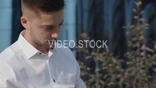 Modern man in white shirt sitting outdoor and holds a tablet computer.