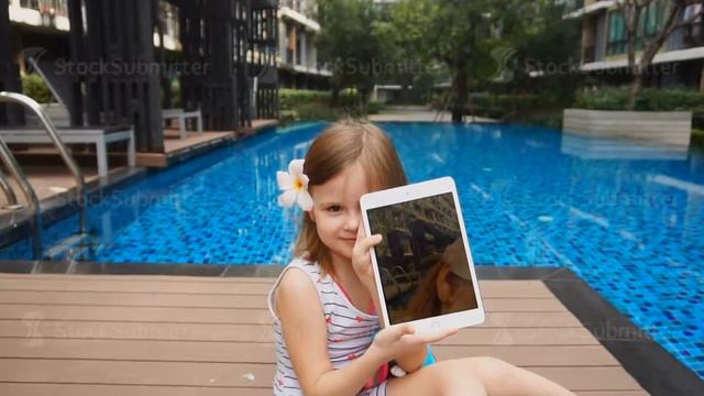 Female kid showing selfie on tablet and sitting near swimming pool.