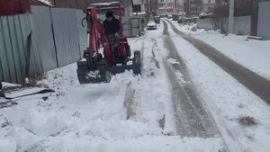 прицепной мини-экскаватор чистит снег