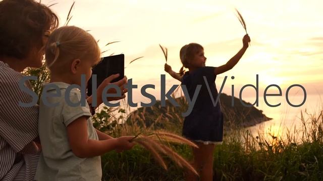 Mother taking pictures with touch pad of her two little daughters at sunset over ocean