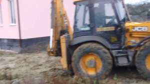 Экскаватор - планировщик JCB 4CX отсыпает и выравнивает грунт на участке.