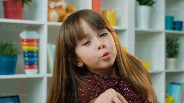Cute little girl blowing kisses at the camera in kids room. White shelves with toys background смотреть онлайн