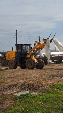 Погрузчик высыпает удобрение из мешков в телегу от трактора