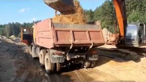 Экскаватор Hitachi 330 отгружает самосвалы камаз песком. The