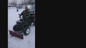 Эл. квадроцикл Фермер отгребает снег от стен здания