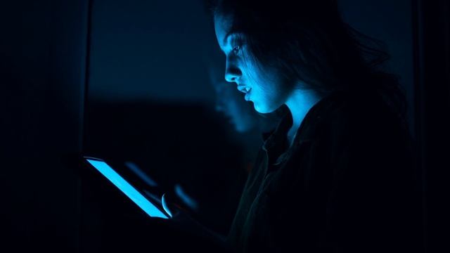 зритель в темном зале смотрит на светящийся экран телефона, проверяя время