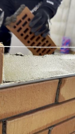Мастер кладет облицовочный кирпич на темный раствор