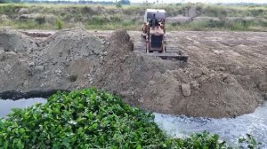 самосвалов Выгружают Грунт в Озеро, Толкая его старым Бульдозером Komatsu