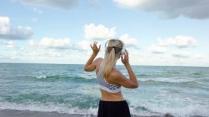 Девушка на пляже в наушниках танцует.