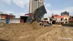 Бульдозер засыпает канаву вдоль дороги песком.