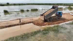 Бульдозер Komatsu толкает грунт для засыпки повреждённого и разрушенного участка дороги.